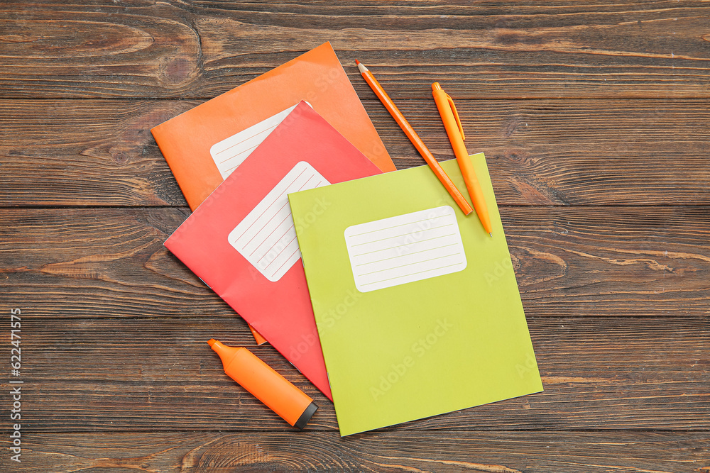 Different colorful notebooks with stationery on brown wooden background