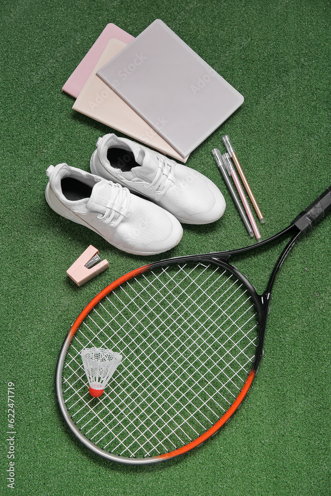 Sneakers with badminton shuttlecock, racket and different stationery on color background