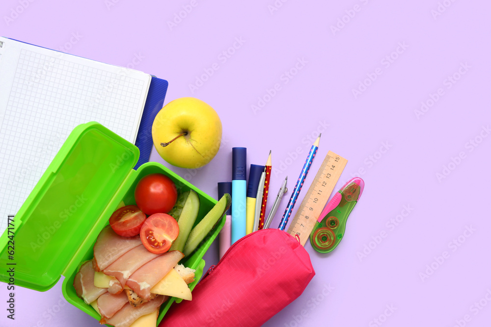 Different stationery and lunch box with tasty food on lilac background