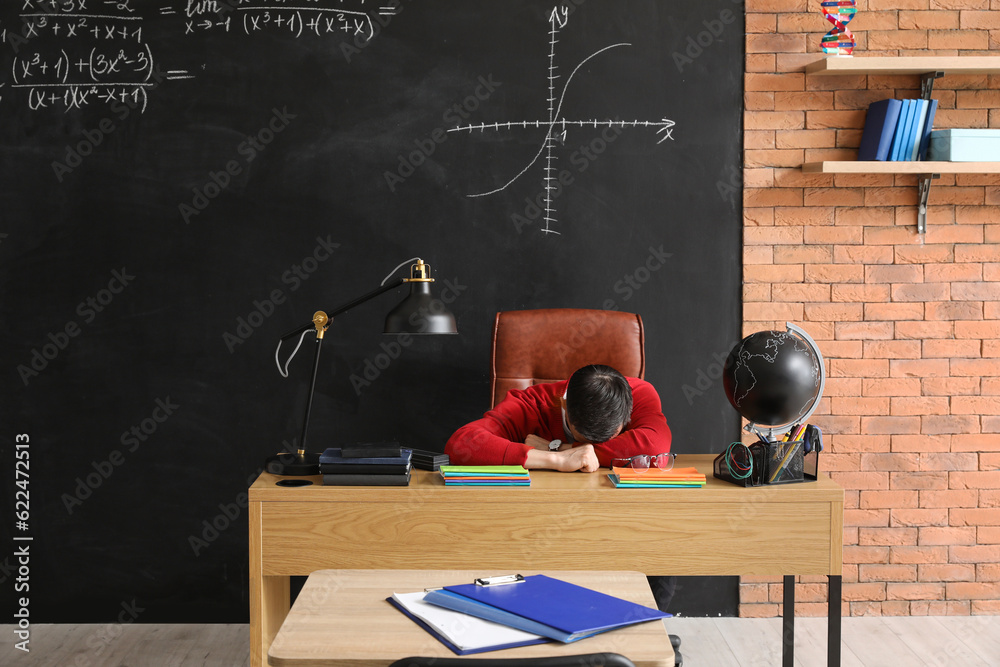 Male teacher sleeping at table in classroom