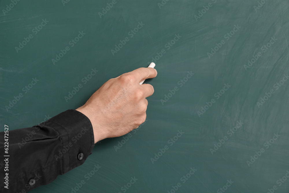 Male teacher writing on chalkboard in classroom, closeup