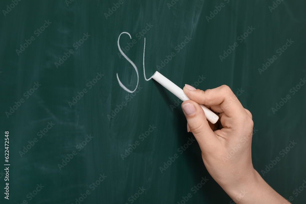 Female teacher writing on chalkboard in classroom, closeup