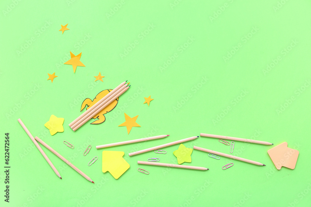 Creative composition with paper rocket, stars and different stationery on green background