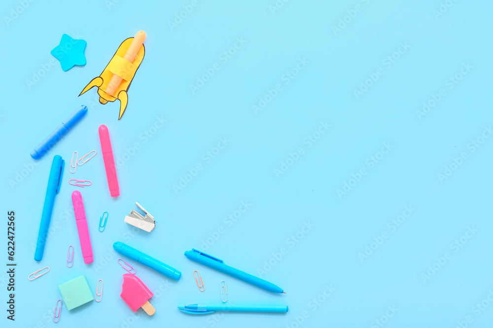 Creative composition with paper rocket and different stationery on blue background