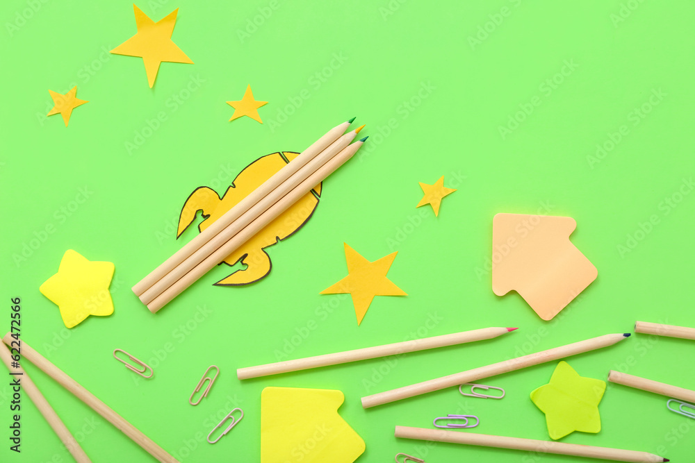 Creative composition with paper rocket, stars and different stationery on green background