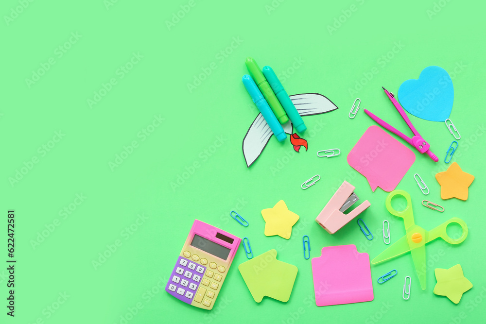 Creative composition with paper rocket, calculator and different stationery on green background