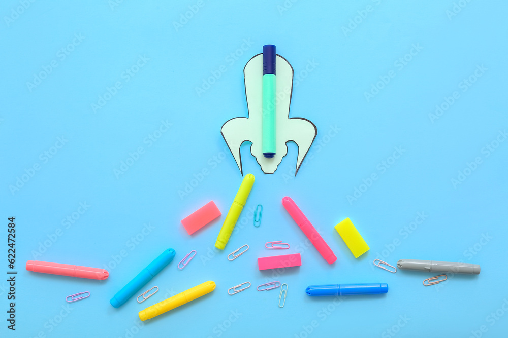 Creative composition with rocket, markers and paper clips on blue background