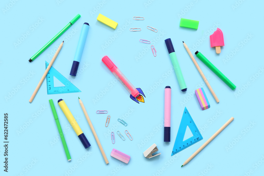 Creative composition with paper rocket and different stationery on blue background