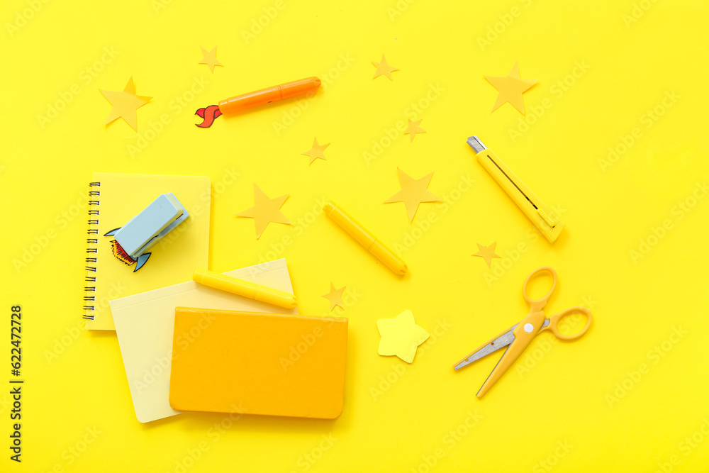 Creative composition with paper rockets, stars and different stationery on yellow background