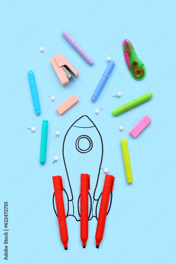 Creative composition with drawn rocket and different stationery on blue background