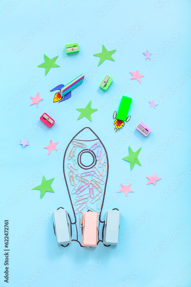 Creative composition with drawn, paper rockets and different stationery on blue background