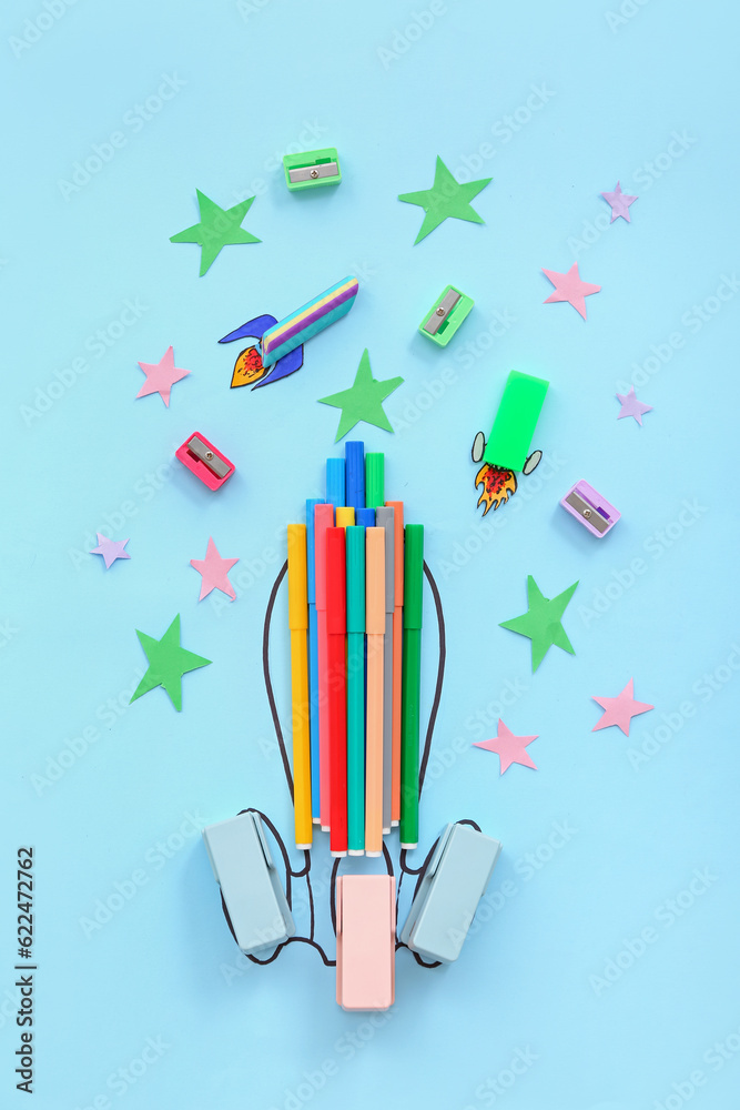 Creative composition with drawn, paper rockets and different stationery on blue background