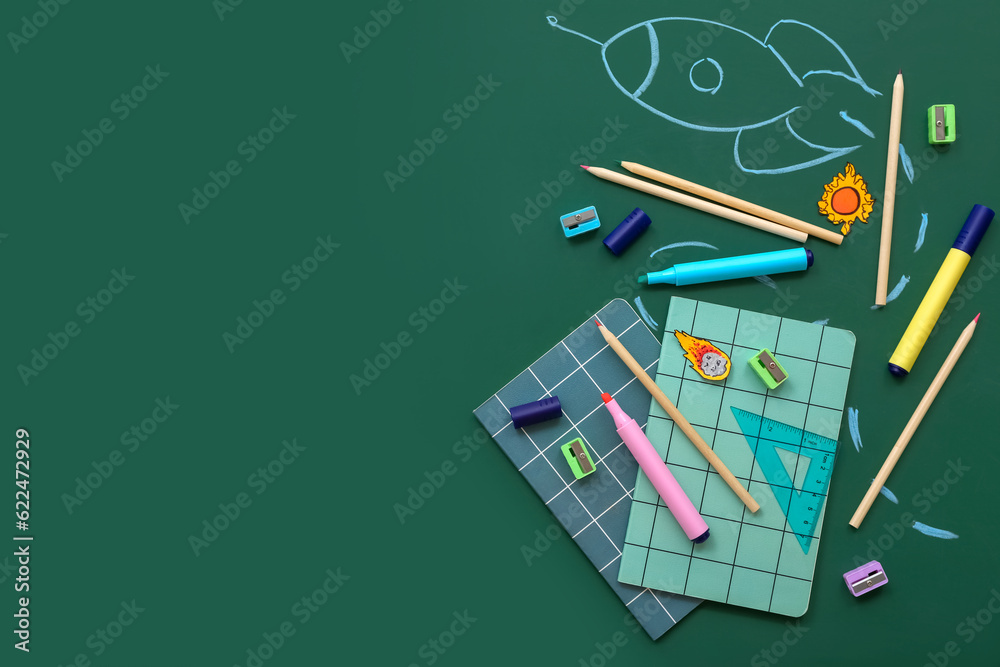 Creative composition with drawn rocket and different stationery on green chalkboard