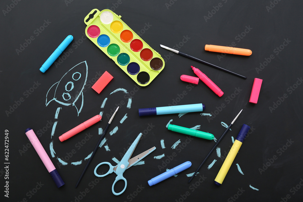 Creative composition with drawn rocket and different stationery on black chalkboard