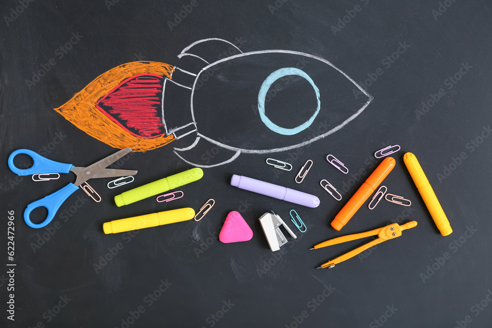 Creative composition with drawn rocket and different stationery on black chalkboard