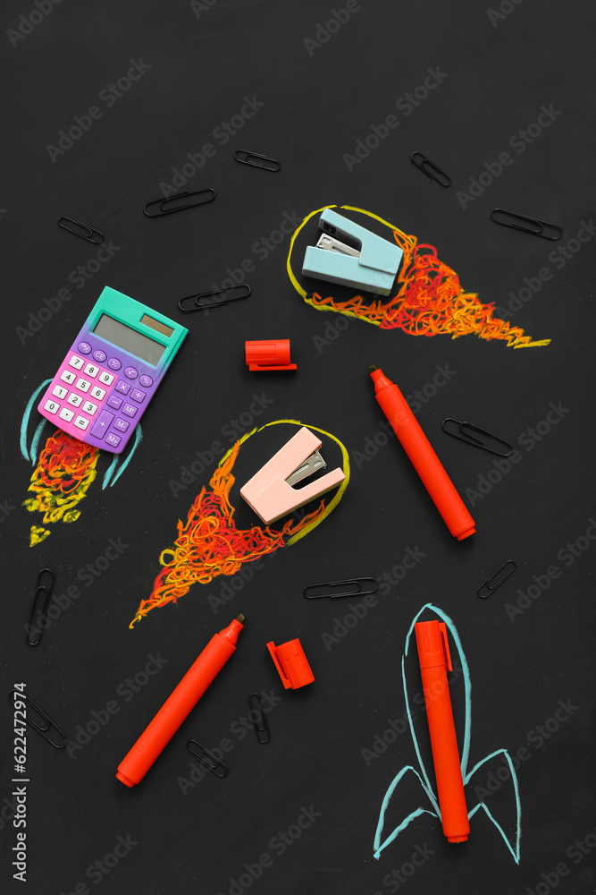 Creative composition with drawn rockets and different stationery on black chalkboard