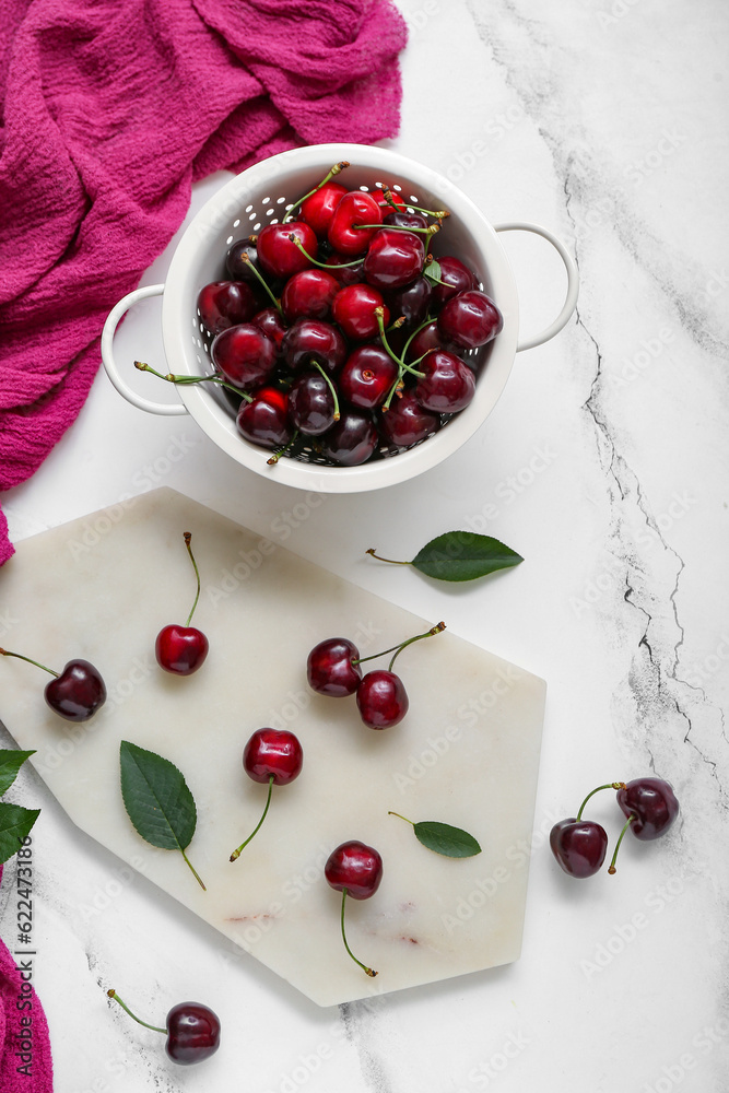 Colander and board with sweet cherries on white background