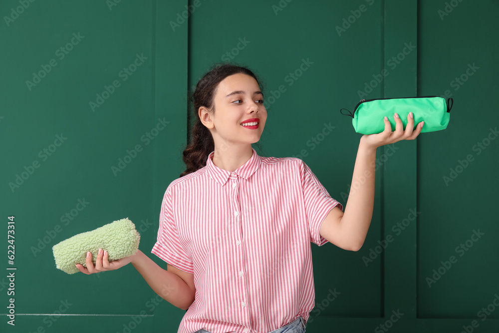 Female student with pencil cases on green background