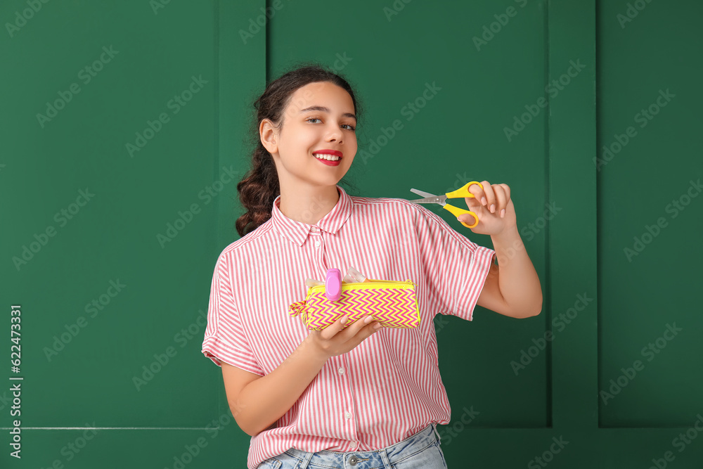 Female student with scissors and pencil case on green background