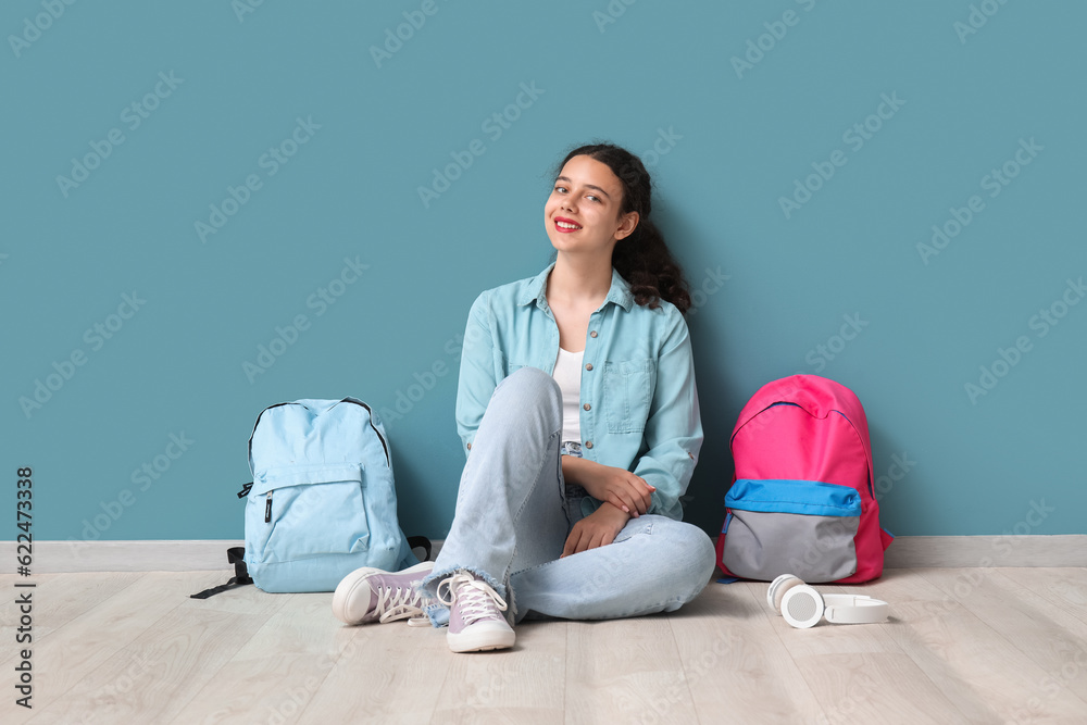 Female student with backpacks sitting near blue wall