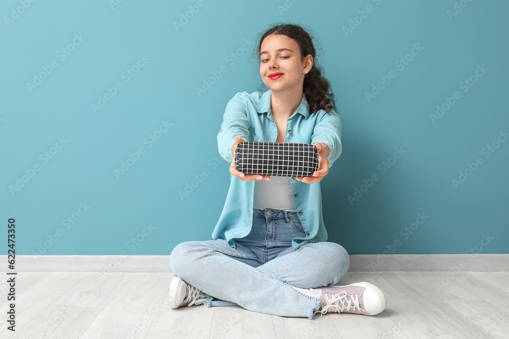 Female student with pencil case sitting near blue wall