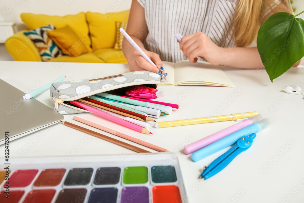 Female student with pencil case writing in copybook at table, closeup