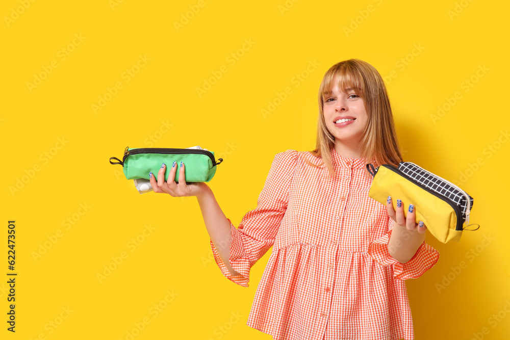 Female student with pencil cases on yellow background