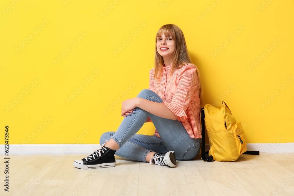 Female student with backpack sitting near yellow wall