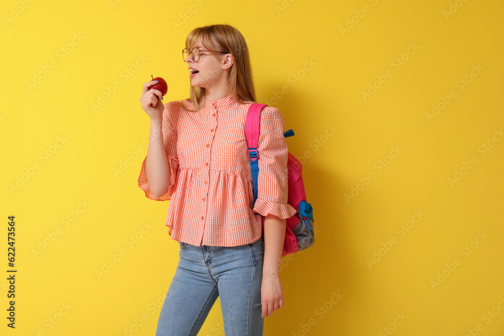 Female student with apple and backpack on yellow background