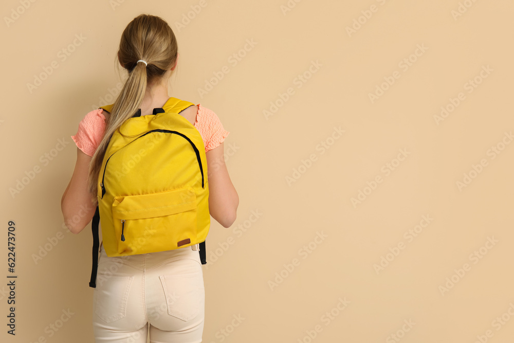 Female student with backpack on beige background, back view