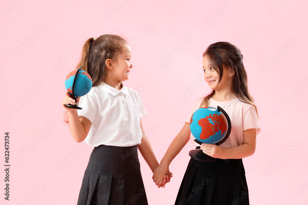 Little schoolgirls with globes on pink background