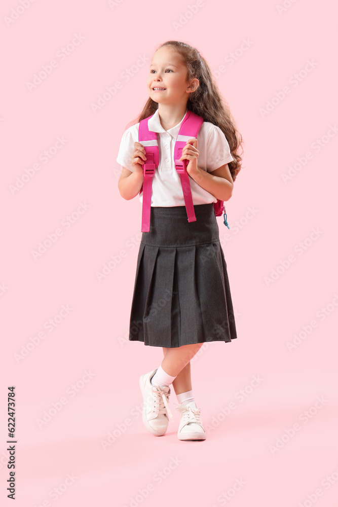 Little schoolgirl with backpack on pink background