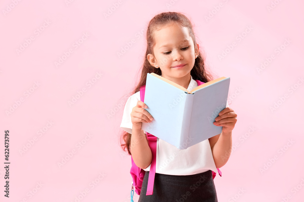 Little schoolgirl with book on pink background