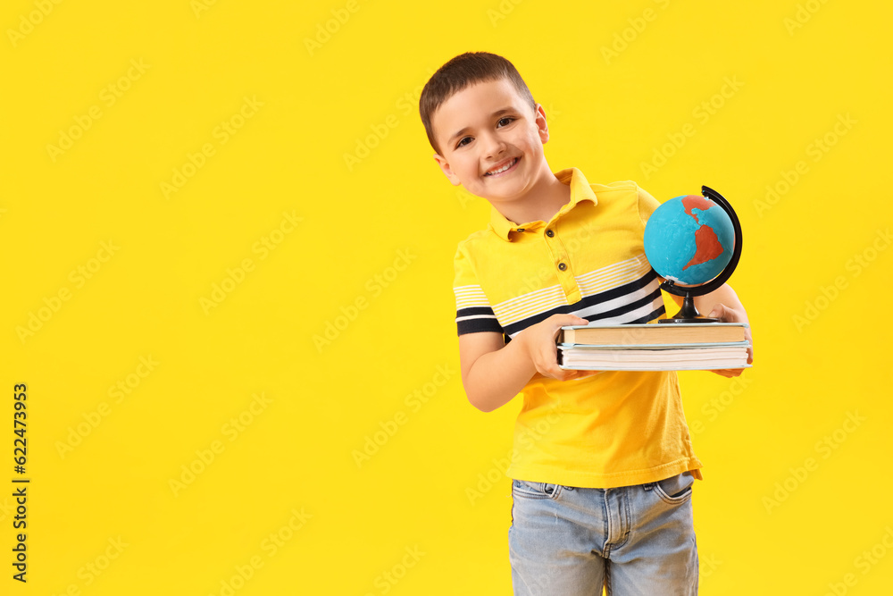 Little schoolboy with books and globe on yellow background