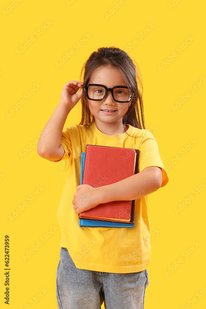 Little schoolgirl with books on yellow background