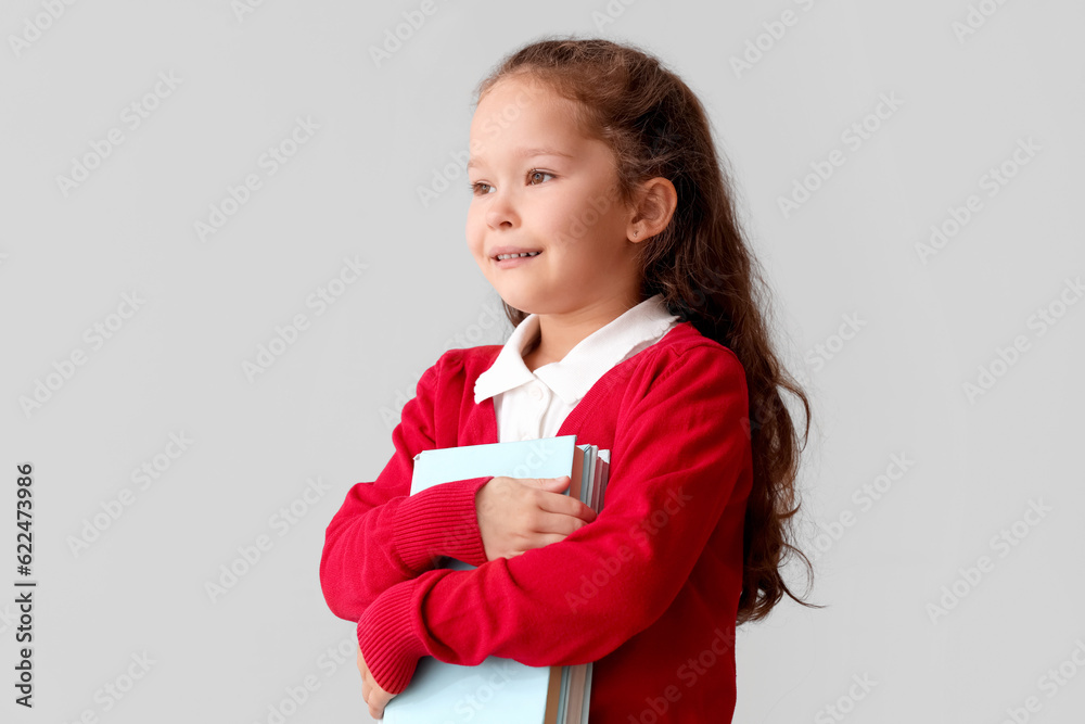 Little schoolgirl with books on grey background