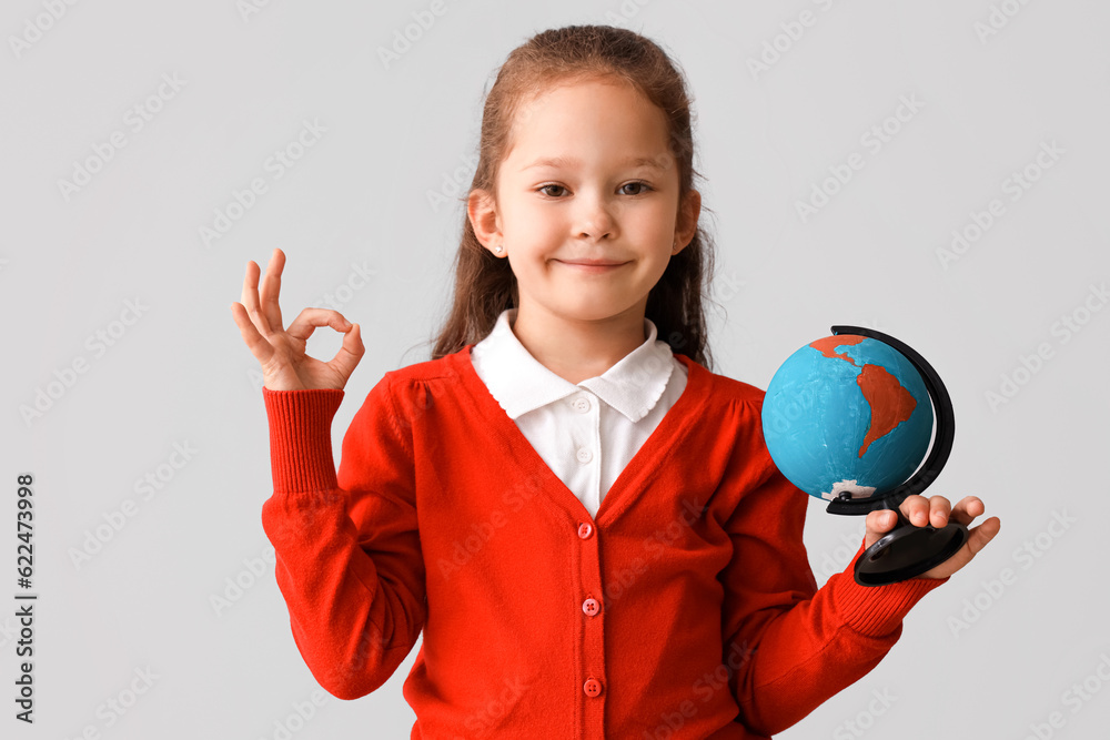 Little schoolgirl with globe showing OK on grey background