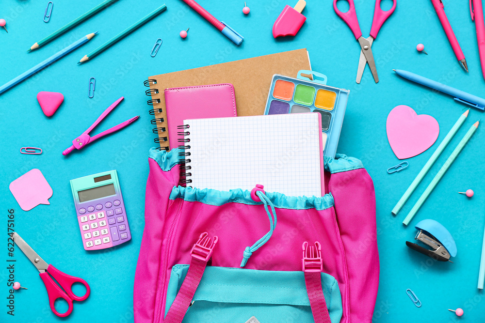 Backpack with blank notebook and different stationery on blue background