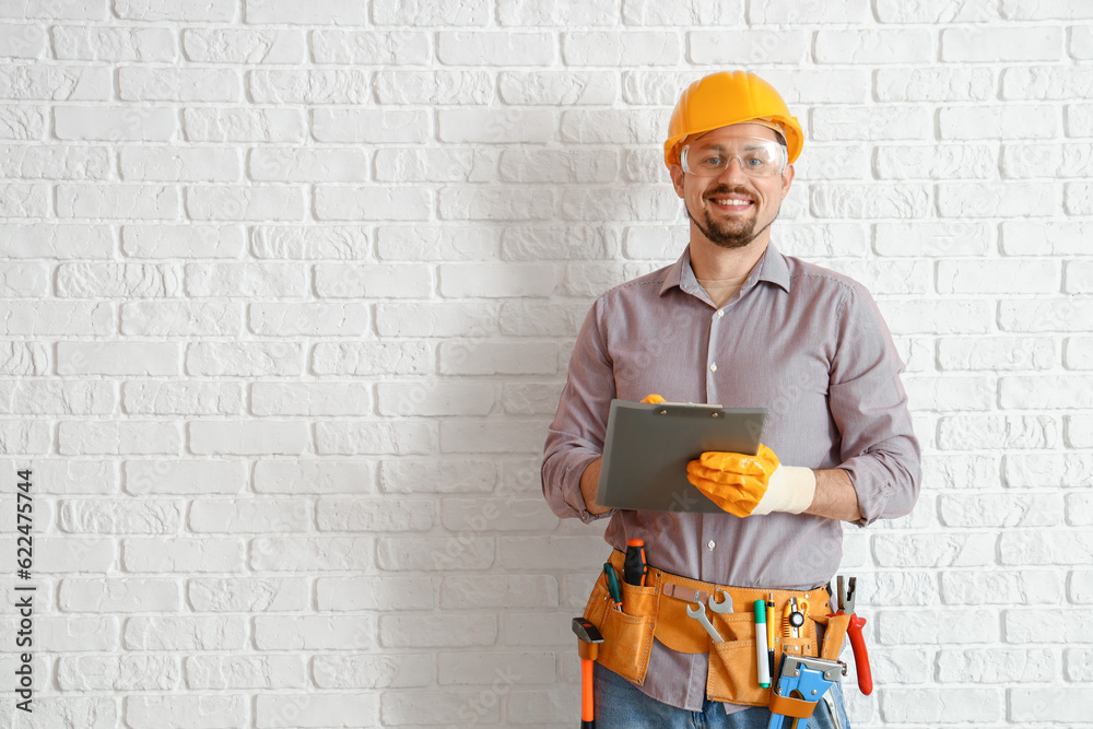 Male builder with clipboard near white brick wall