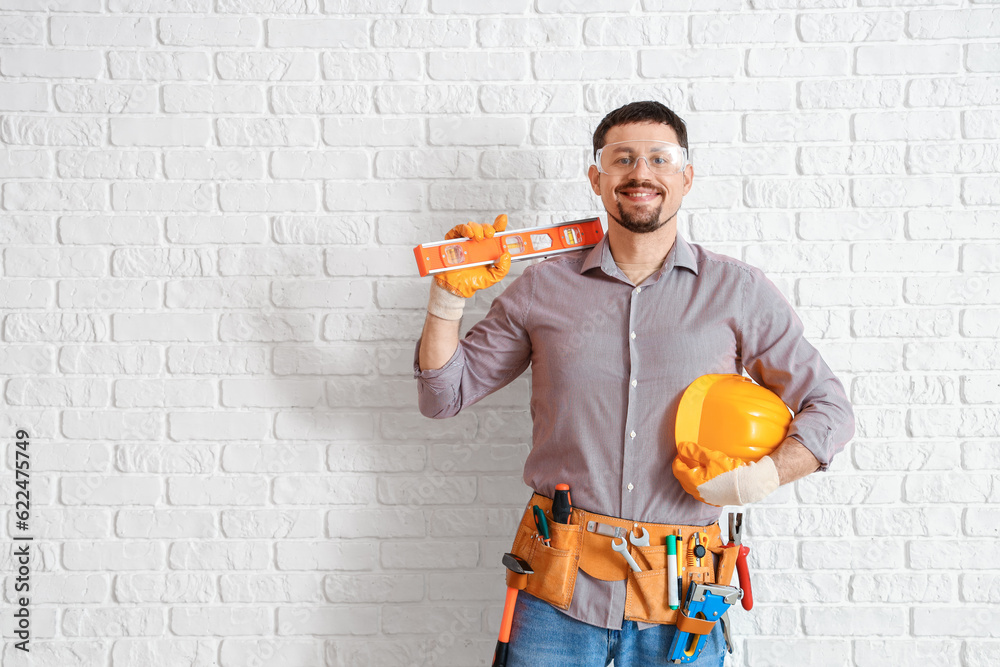 Male builder with tools near white brick wall