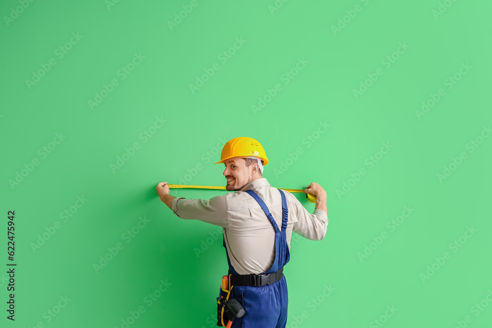 Male builder measuring green wall, back view