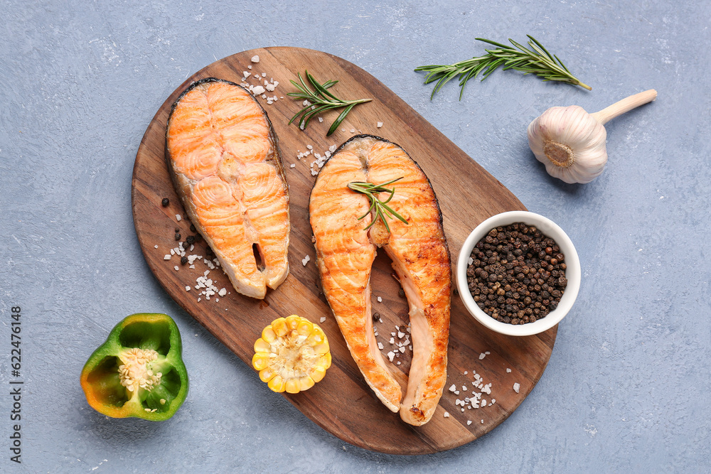 Wooden board with tasty grilled salmon steaks on blue background