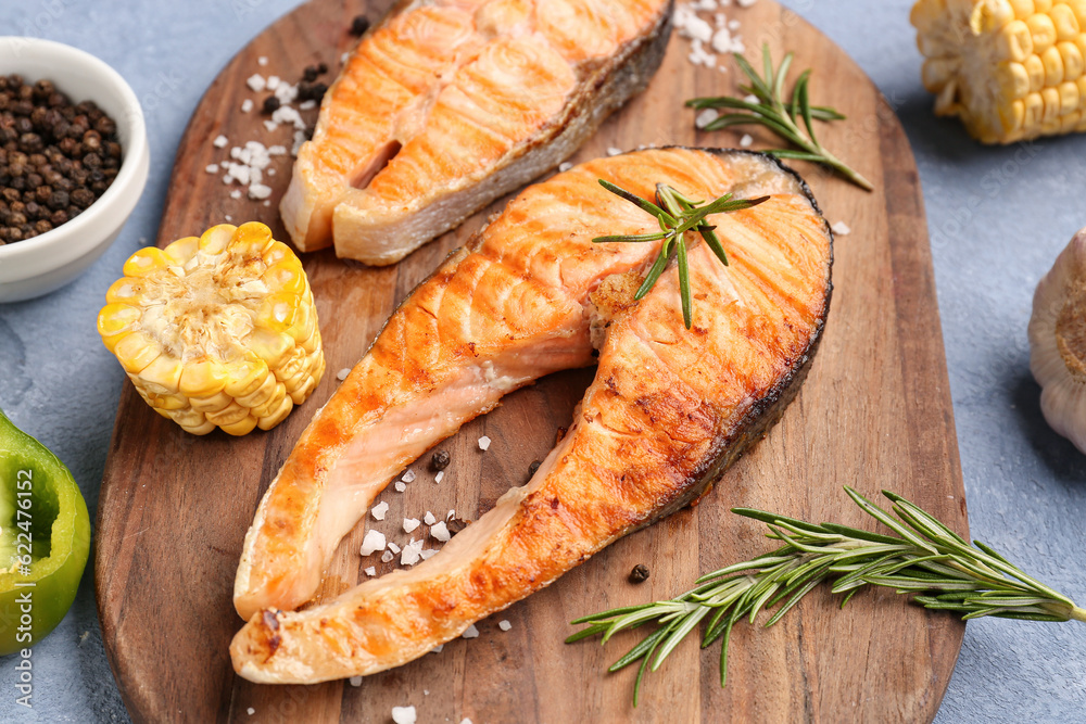 Wooden board with tasty grilled salmon steaks on blue background