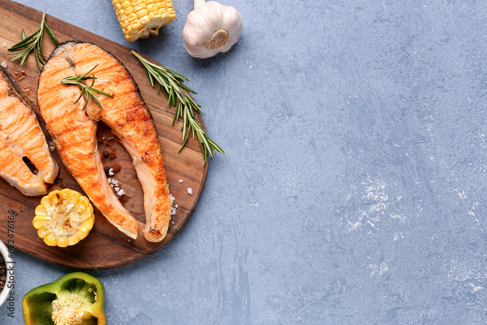 Wooden board with tasty grilled salmon steaks on blue background