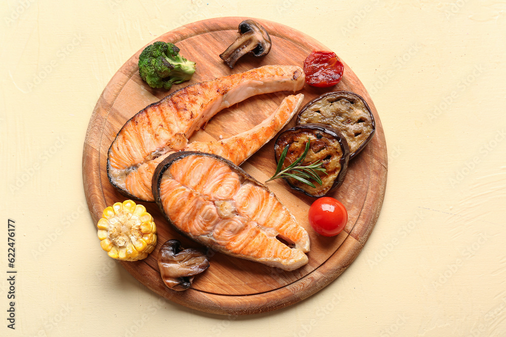 Wooden board with tasty grilled salmon steaks and vegetables on yellow background