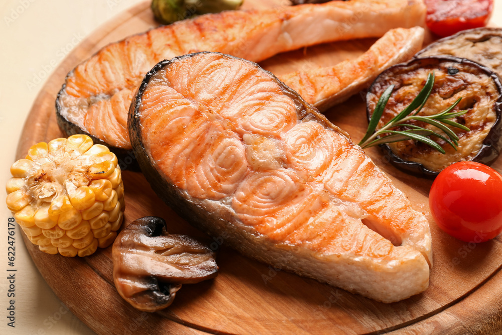 Wooden board with tasty grilled salmon steaks and vegetables on yellow background