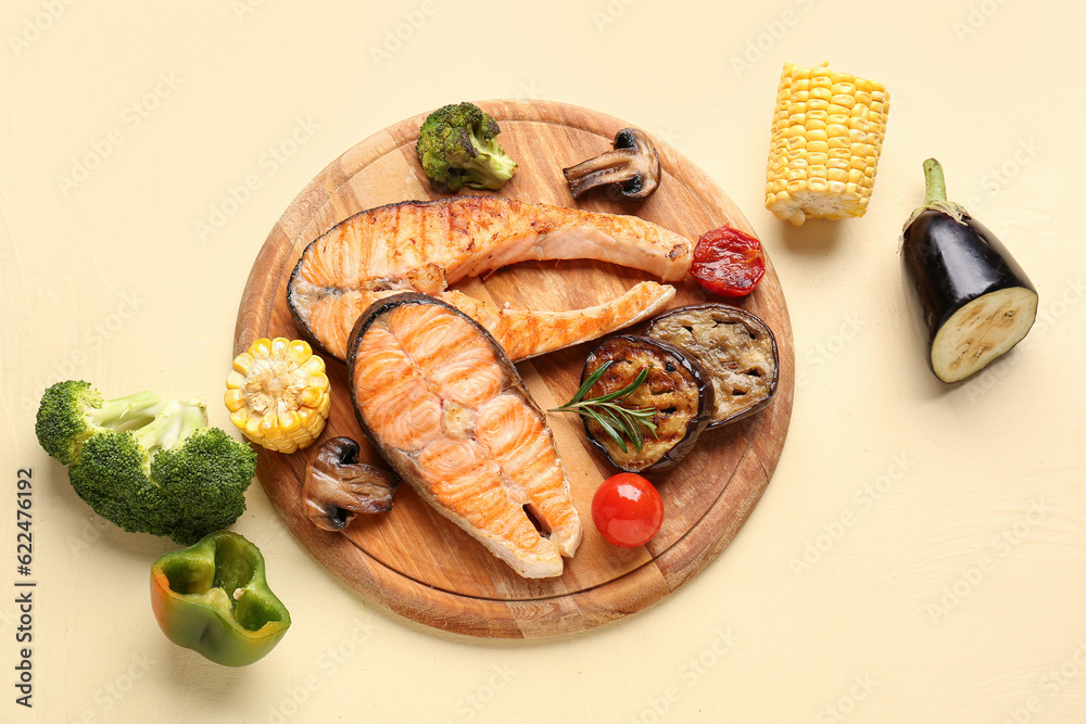 Wooden board with tasty grilled salmon steaks and vegetables on yellow background