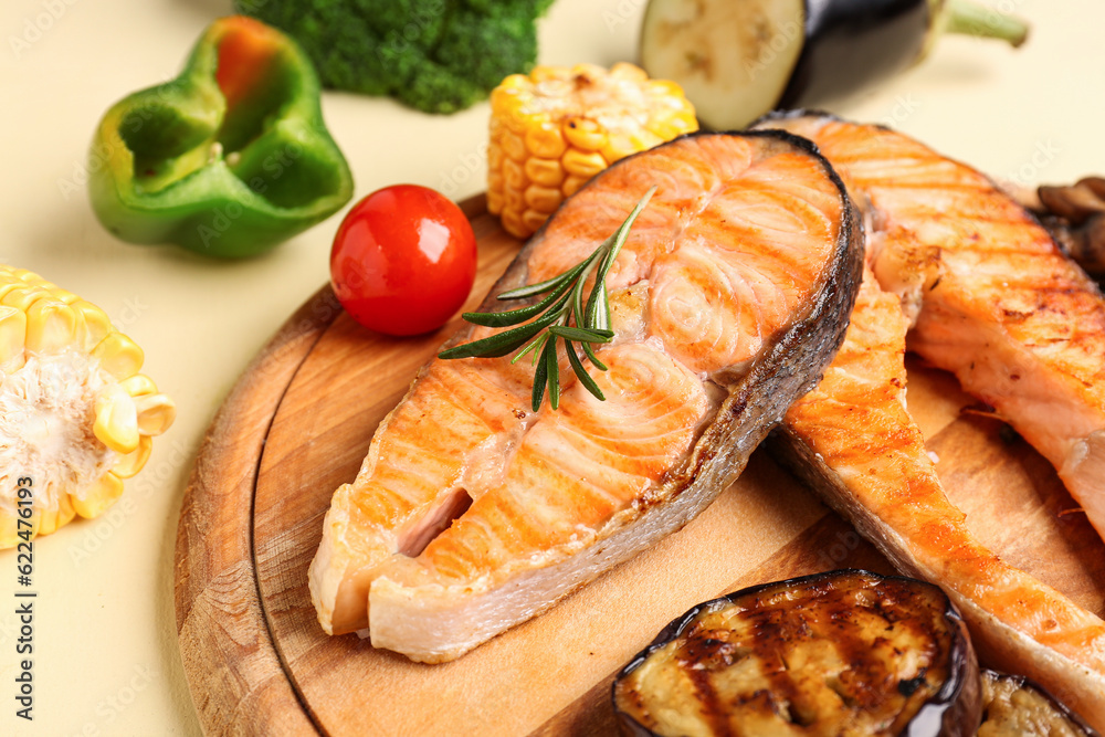 Wooden board with tasty grilled salmon steaks and vegetables on yellow background