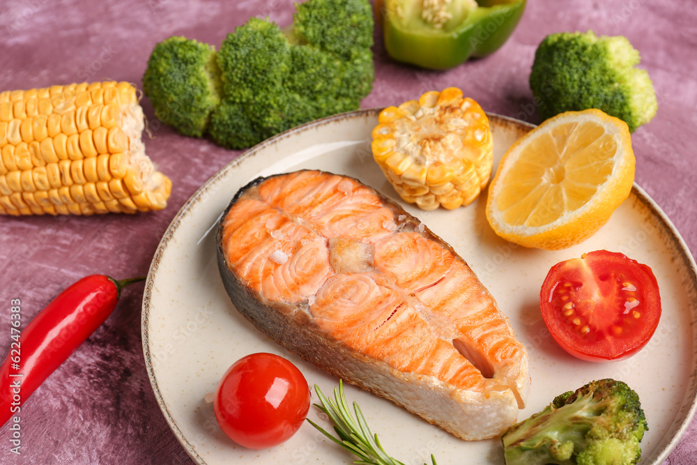 Plate with tasty grilled salmon steak, lemon and vegetables on purple background