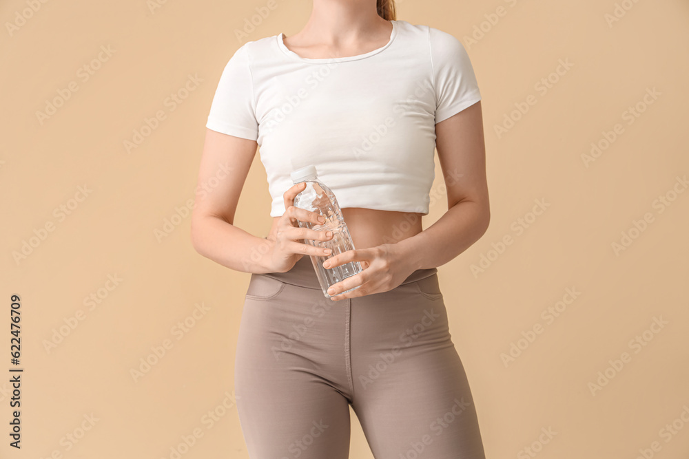 Young woman in sportswear and with bottle of water on  beige background